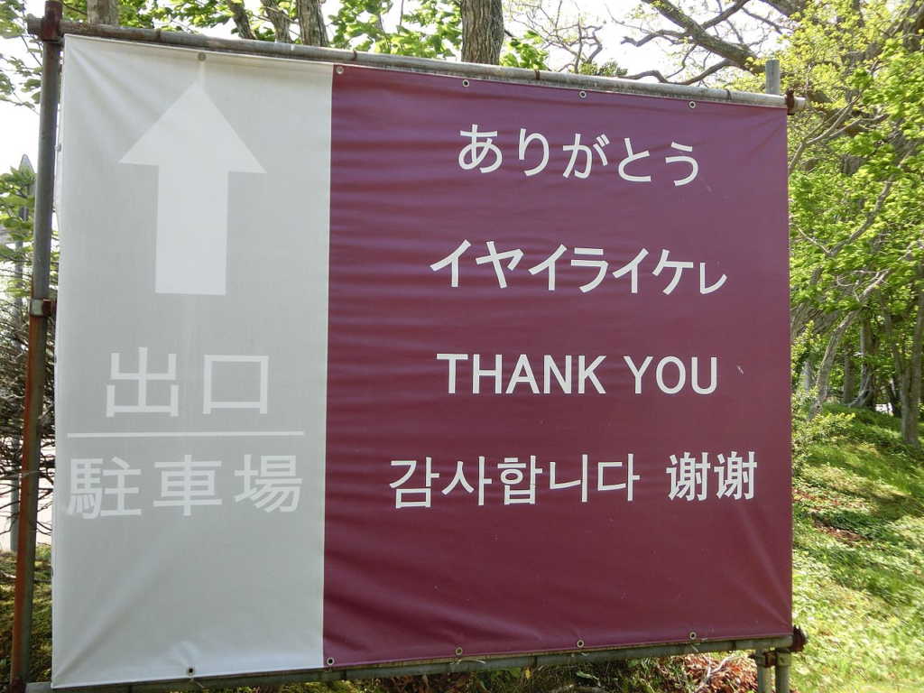 A multilingual sign outside of the Ainu Museum (Shiraoi). It features texts in Japanese, Ainu, English, Korean, and Chinese. The Ainu text, in katakana, is second down from the top on the right side of the sign. It reads イヤイライケㇾ (iyairaiker), meaning "thank you". Picture from Wikipedia. Japan Fans. Japanese Arts & Culture from the Centre of Utrecht.